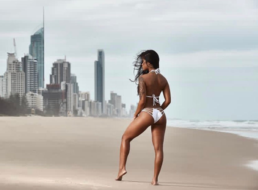 Back view of MissManeater white reefKNOT strappy bikini pant worn on beach with city skyline Australian made designer swimwear